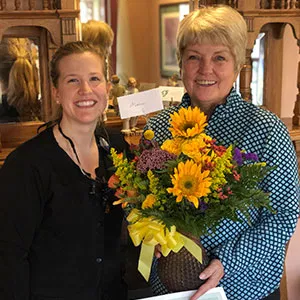 A female staff member posing indoors with a smiling patient receiving a certificate and a large arrangement of sunflowers.