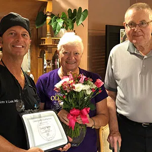 Dr. John Louis standing with a smiling female patient who is holding a gift basket and a Patient of the Month certificate.